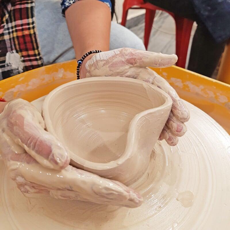 Image of a student working on Potter's Wheel at Sona Pottery. The shape of the pot is in the shape of a heart