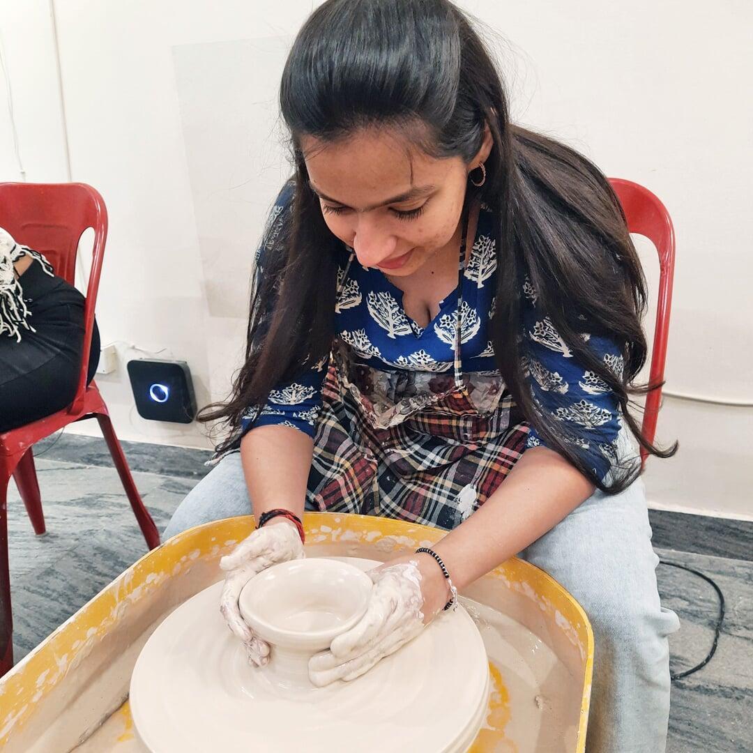 A girl shaping her first creation, a clay cup on potter's wheel. The girl is similing and enjoying the expereince at Sona Pottery