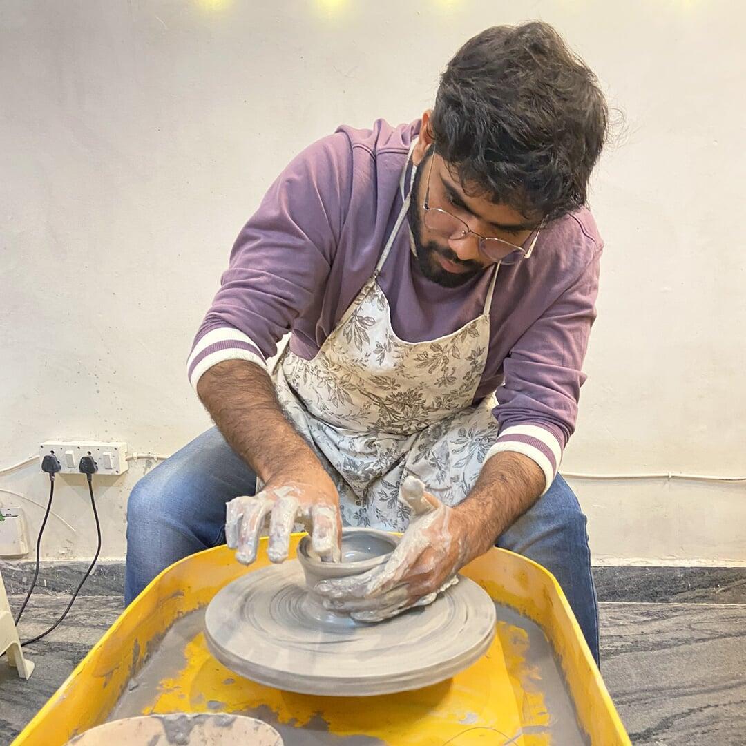 A male participant engrossed in pulling a mug on potter's wheel